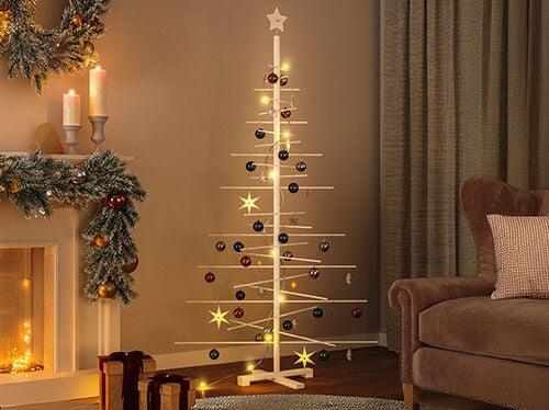 Wooden Christmas tree decorated with baubles, stars and lights, with gift boxes beside it. An armchair and a fireplace with a garland and lit candles in a styled living room. Click to see the products in the collection.