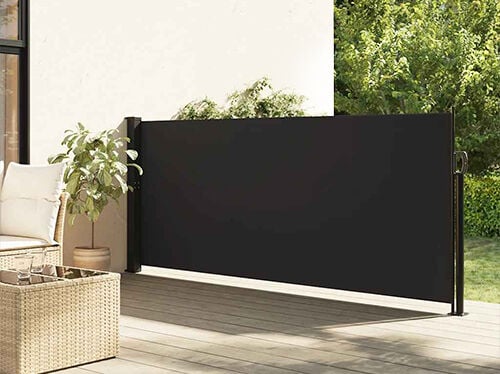 Retractable black side awning installed on a styled patio beside outdoor seating and a potted plant. Click to see the products in the collection.