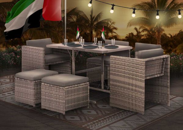 Outdoor rattan dining set with chairs and stools arranged for dinner under string lights at night, with UAE flags on the table. 