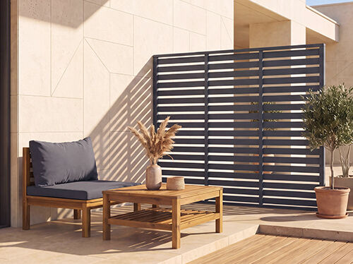 Modern outdoor patio with a wooden lounge chair, coffee table, potted plants and a dark privacy fence.