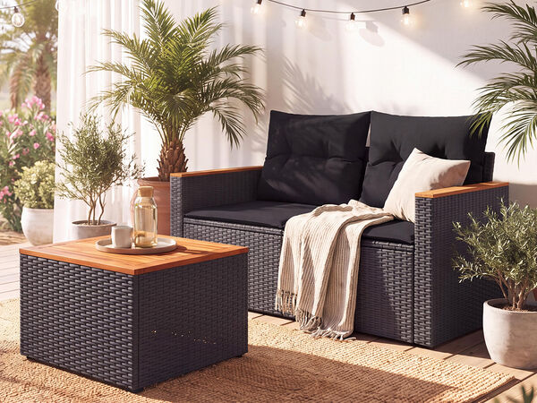 Stylish black rattan outdoor seating with a wooden coffee table, cushions and tropical plants in a bright outdoor space
