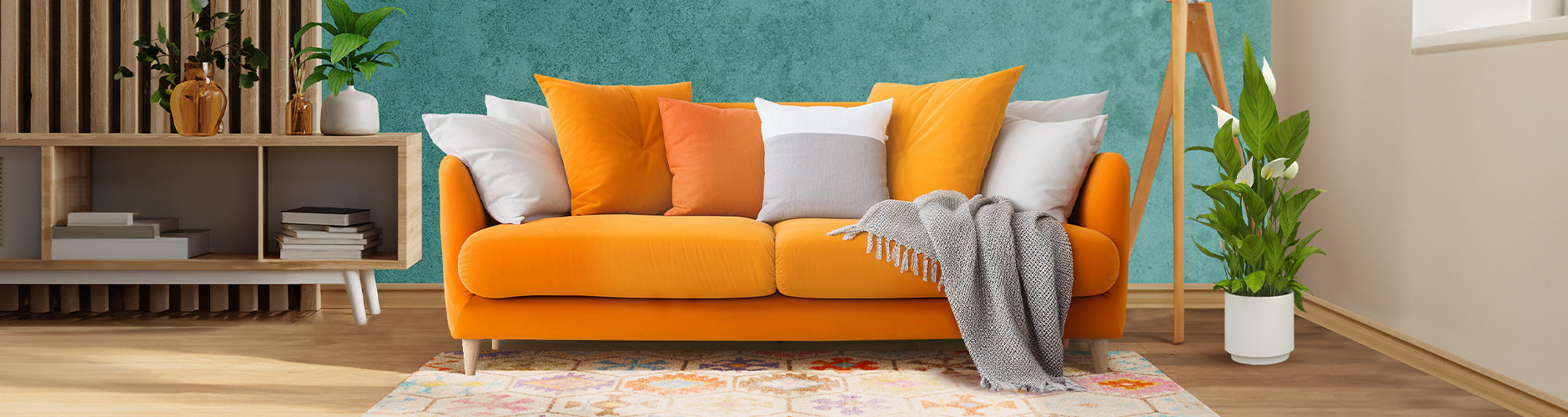 Orange sofa, colorful pillows, and a grey throw blanket. A wooden TV cabinet, potted plant, and floor lamp in a styled living space.