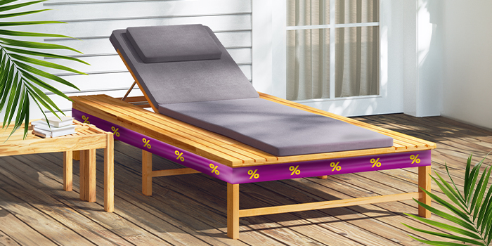 Wooden sun lounger with a grey cushion and a purple promotional band with yellow discount icons, on a wooden deck. Click to shop the collection.